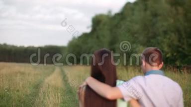 一个男人和一个女孩拥抱沿着乡村的道路到田野。 日落，夏天。